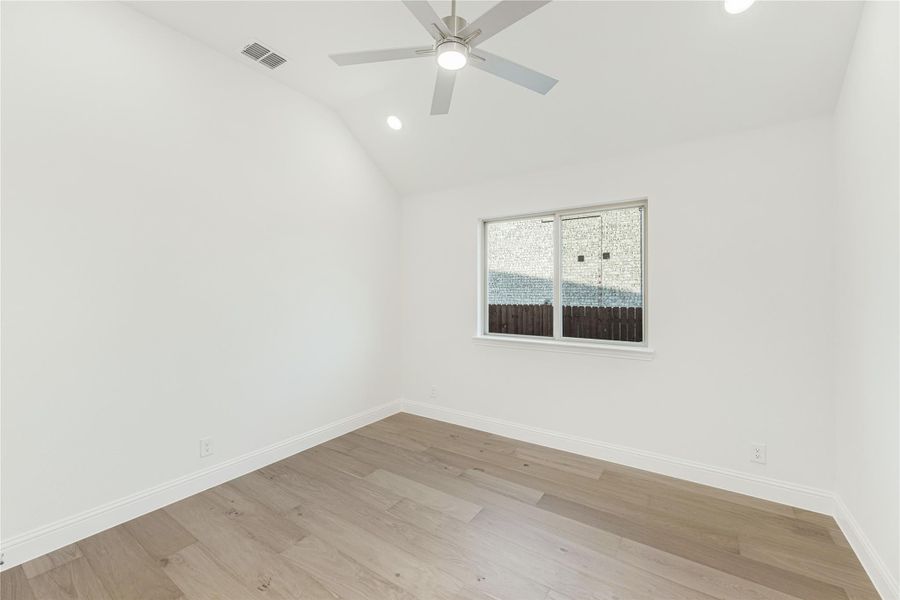 Empty bedroom with vaulted ceiling, ceiling fan, hardwood floors, and single window