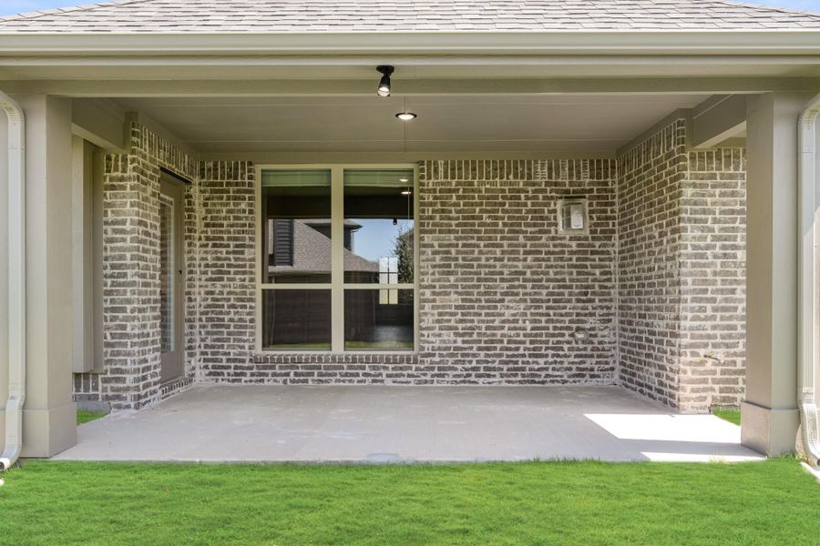 Covered back patio with concrete floor, brick walls, ceiling lights, and large window overlooking green lawn