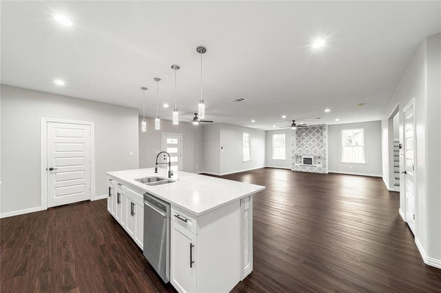 Kitchen with a ceiling fan, open floor plan, a large fireplace, an island with sink, and dark wood-type flooring