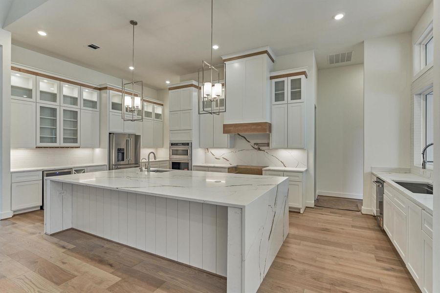 Showcase kitchen with a grand waterfall island, stainless steel appliances, lighted upper cabinets, and elegant quartz finishes—an entertainer’s dream."