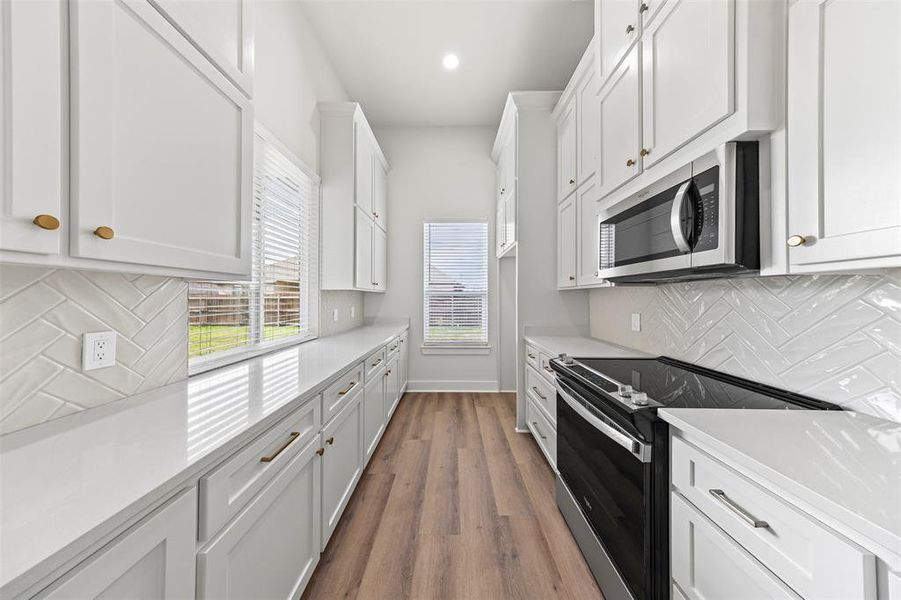 Kitchen with decorative backsplash, electric range oven, stainless steel microwave, white cabinets, and recessed lighting Kitchen with decorative backsplash, electric range oven, stainless steel microwave, white cabinets, and recessed lighting