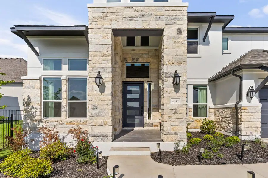 Contemporary facade featuring a stone veneer entryway with sleek black sconces, a dark paneled entry door, and multi-paned windows