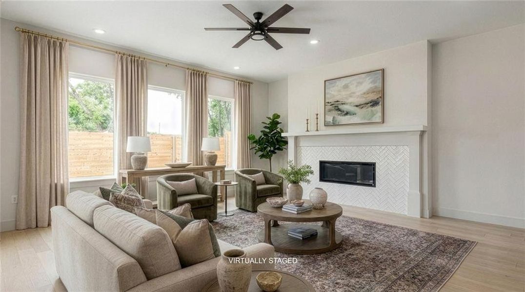 Spacious interior with light wood-finish flooring, a modern fireplace with a herringbone tile surround and white mantel, recessed lighting, and a ceiling fan. Spacious interior with light wood-finish flooring, a modern fireplace with a herringbone tile surround and white mantel, recessed lighting, and a ceiling fan.