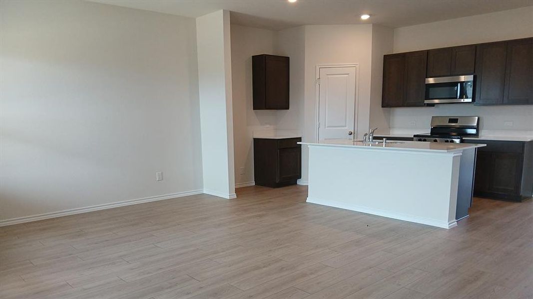 Contemporary kitchen featuring dark wood cabinetry, stainless steel appliances, a center island with a double basin sink, and wood-finish flooring Contemporary kitchen featuring dark wood cabinetry, stainless steel appliances, a center island with a double basin sink, and wood-finish flooring