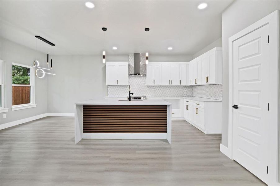 Kitchen featuring an island with sink, white cabinetry, light hardwood / wood-style floors, and wall chimney range hood