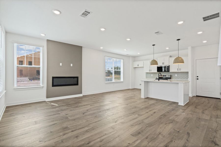 Wood-finish flooring, recessed lighting, and an electric fireplace feature in this open living space
