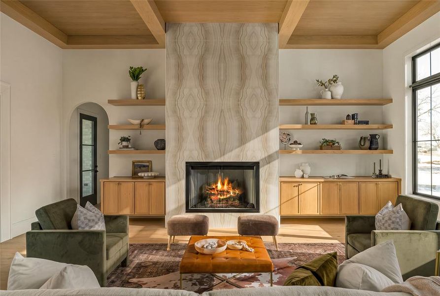 Living space featuring a stone-clad fireplace, coffered wood-finish ceiling, and built-in shelving with cabinetry