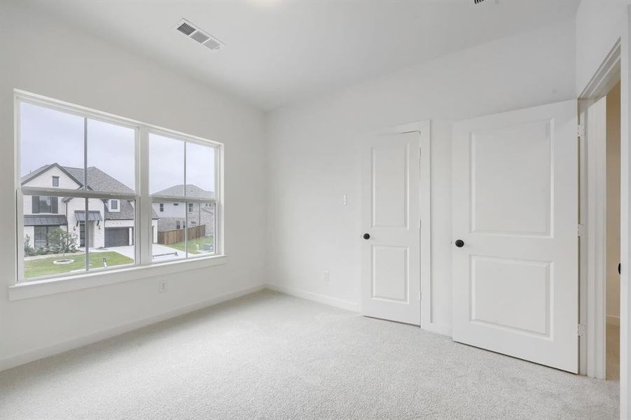 Bright room featuring light gray carpeting, a large multipane window, white trim, two white two-panel doors with black hardware, and an overhead ventilation register