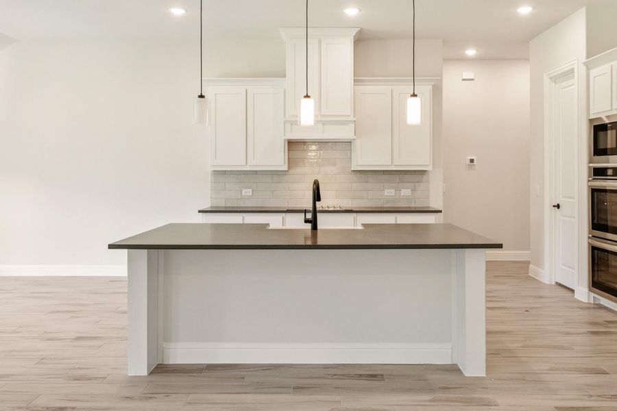 Kitchen with large island, dark countertops, white cabinets, subway tile backsplash, and pendant lights