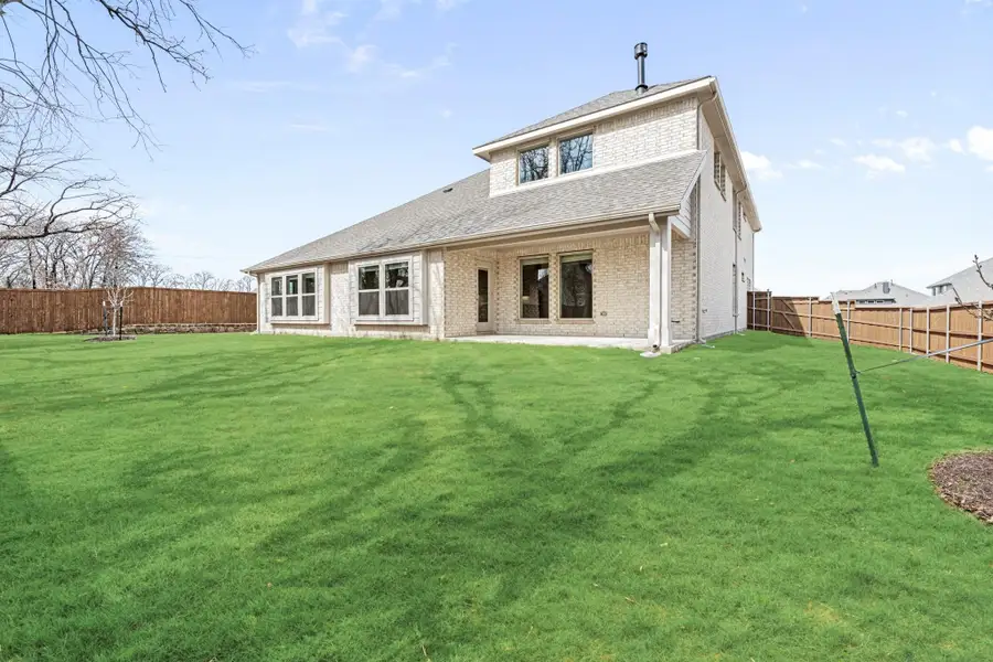 Rear view of two-story brick home with large fenced backyard and green lawn
