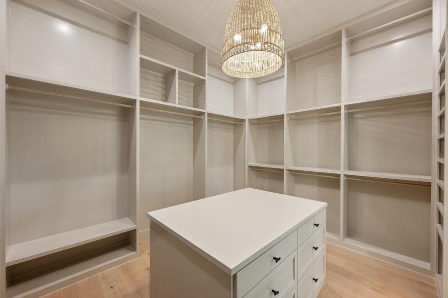 An organized closet featuring ample shelving, hanging space, and a functional center island. An organized closet featuring ample shelving, hanging space, and a functional center island.