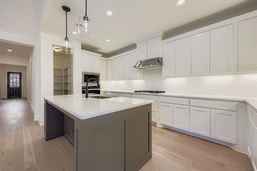 Kitchen with white cabinetry, tasteful backsplash, light wood-style floors, a center island with sink, and recessed lighting Kitchen with white cabinetry, tasteful backsplash, light wood-style floors, a center island with sink, and recessed lighting