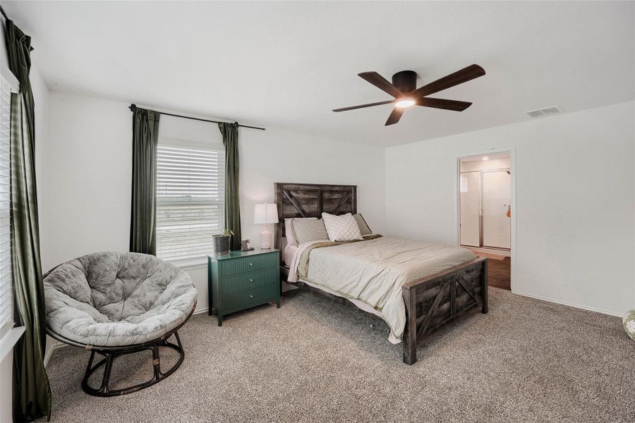 Carpeted room featuring a ceiling fan with integrated lighting, window with blinds, and an open doorway to a bathroom with a shower enclosure Carpeted room featuring a ceiling fan with integrated lighting, window with blinds, and an open doorway to a bathroom with a shower enclosure