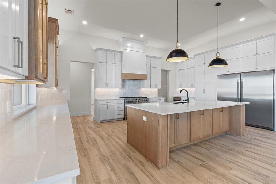 Kitchen with an island with sink, high quality appliances, light wood-style floors, white cabinets, and light stone countertops Kitchen with an island with sink, high quality appliances, light wood-style floors, white cabinets, and light stone countertops