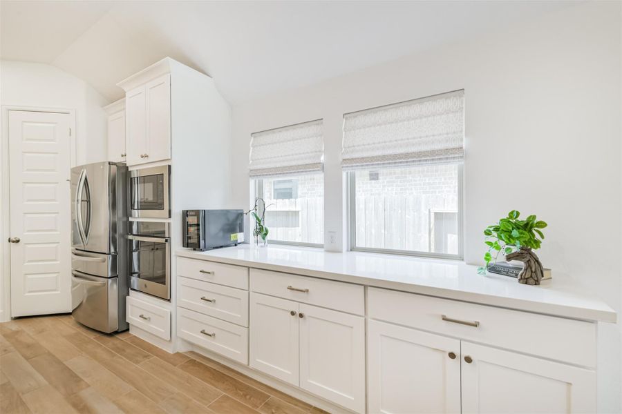 Extra cabinets and quartz counters line the wall of the dining area, lit by large windows with custom shades. Extra cabinets and quartz counters line the wall of the dining area, lit by large windows with custom shades.
