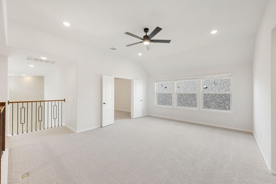 Spacious bedroom with vaulted ceiling, ceiling fan, carpet flooring, and staircase railing nearby