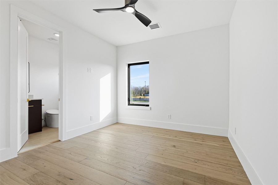 Same floorplan - different finishes. Secondary bedroom featuring light-oak wide-plank flooring, a matte black ceiling fan, and large windows for natural light.