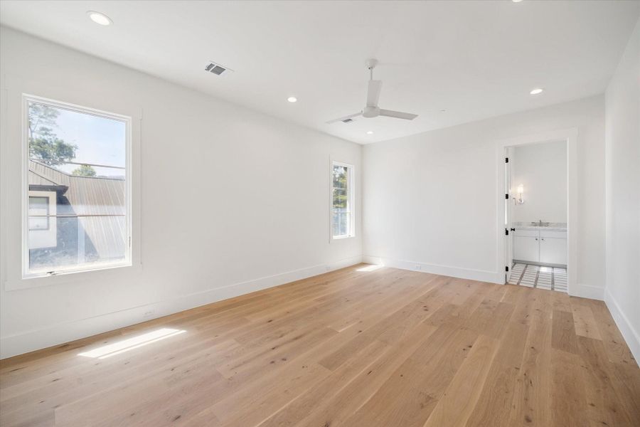 This is a bright and spacious room with light wooden floors, white walls, and recessed lighting. It features two windows for natural light, a ceiling fan, and an en-suite bathroom with modern fixtures. This is a bright and spacious room with light wooden floors, white walls, and recessed lighting. It features two windows for natural light, a ceiling fan, and an en-suite bathroom with modern fixtures.