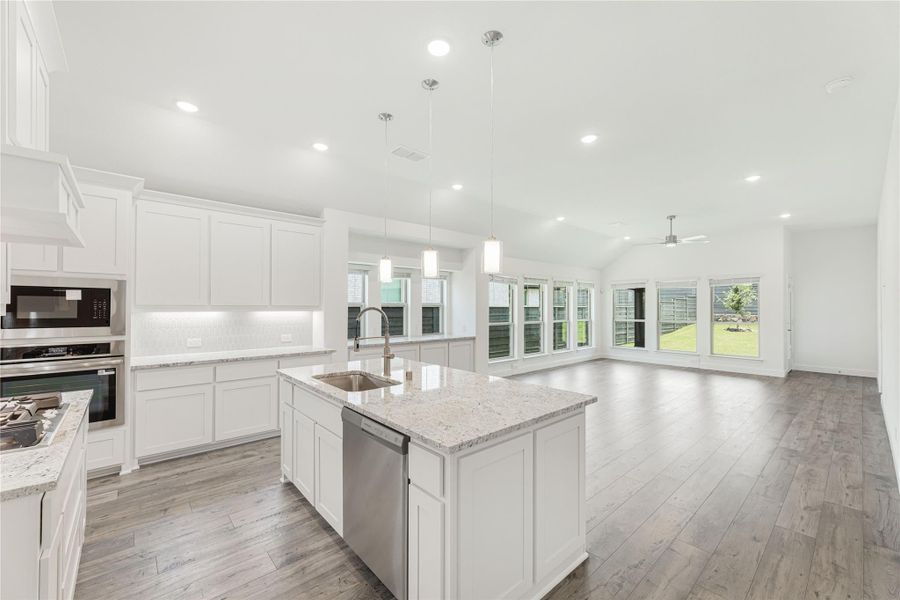 Open kitchen with white cabinets, granite island, stainless appliances, and hardwood floors opening to living area. Open kitchen with white cabinets, granite island, stainless appliances, and hardwood floors opening to living area.