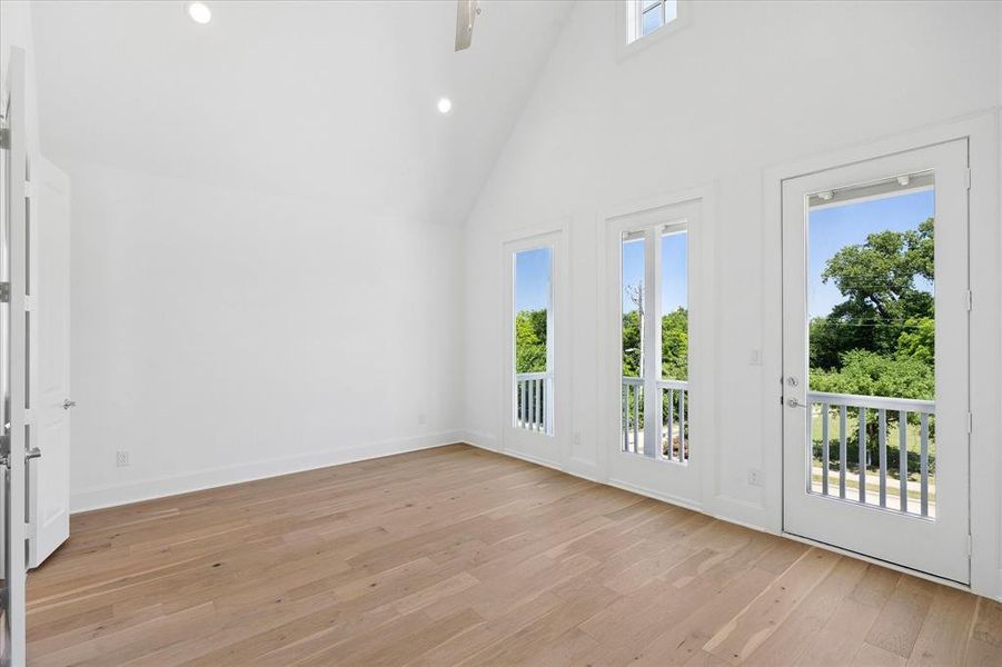 Spacious room featuring vaulted ceilings, recessed lighting, wood-finish flooring, and multiple French doors opening to balconies with white railings