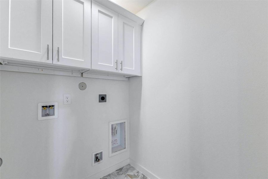 Utility room with white upper cabinetry, washer and dryer connections, and a clean neutral finish. The built-in storage and dedicated laundry hookups add everyday convenience while keeping household tasks organized and tucked away.