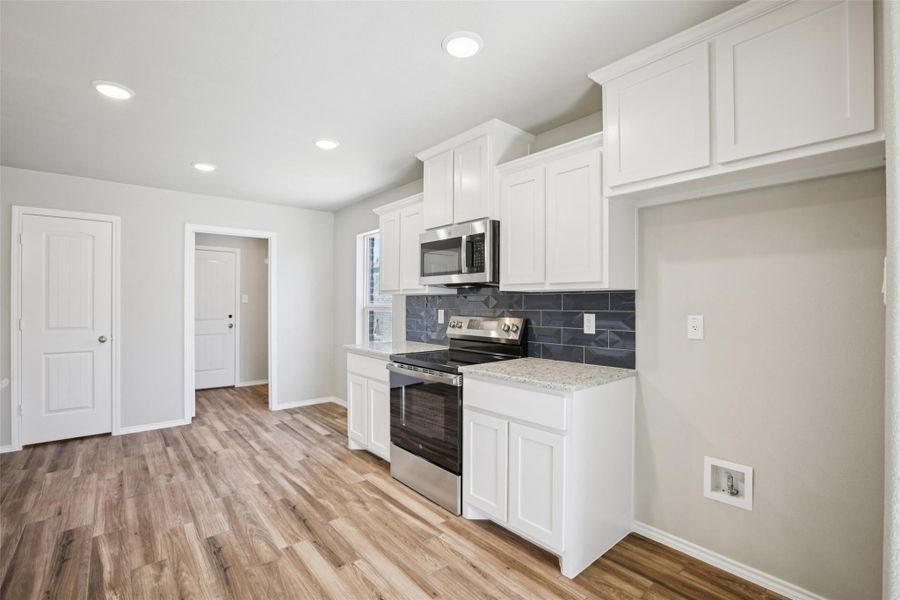 Kitchen featuring stainless steel appliances, white cabinets, tasteful backsplash, light stone counters, and light wood-type flooring