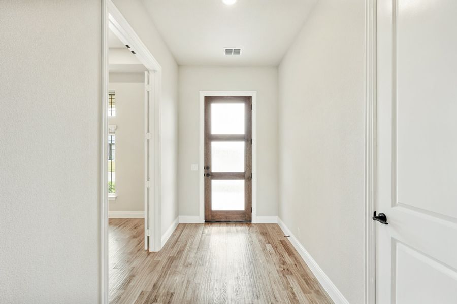 Hallway with light wood floors, white walls, and a wood-framed glass panel door at the end Hallway with light wood floors, white walls, and a wood-framed glass panel door at the end
