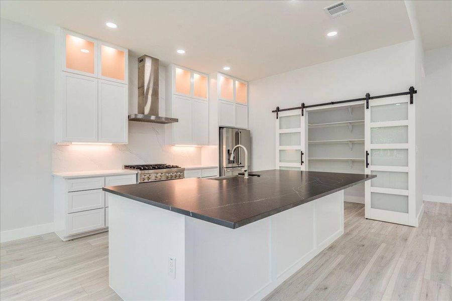 Kitchen featuring range exhaust hood, pantry with barn door, light wood finished floors, high end fridge, and white cabinets Kitchen featuring range exhaust hood, pantry with barn door, light wood finished floors, high end fridge, and white cabinets