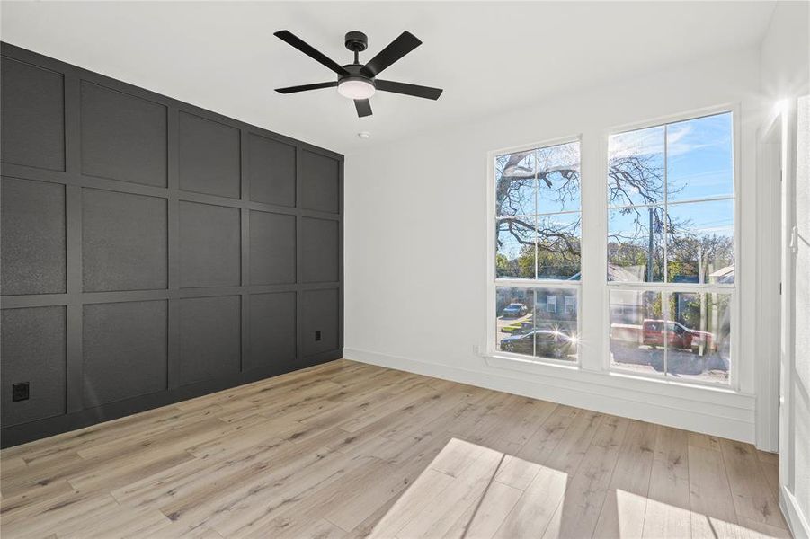 Unfurnished bedroom featuring a decorative wall, light wood-style flooring, and a ceiling fan