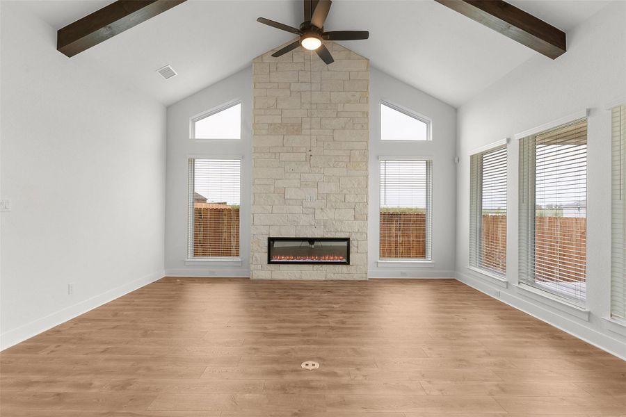 Unfurnished living room featuring a stone fireplace, light wood-style flooring, a ceiling fan, healthy amount of natural light, and beamed ceiling