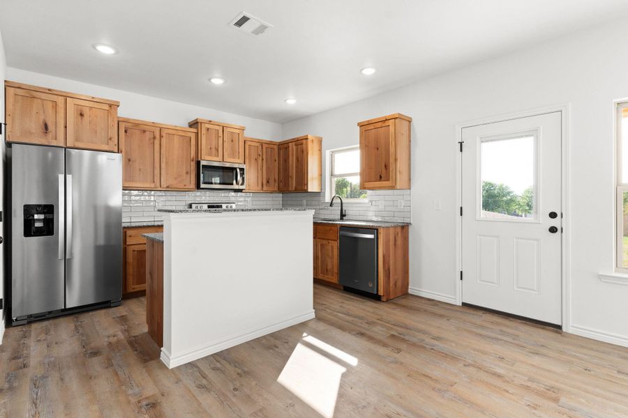 Kitchen with stainless steel appliances, tasteful backsplash, visible vents, and light wood-style flooring Kitchen with stainless steel appliances, tasteful backsplash, visible vents, and light wood-style flooring