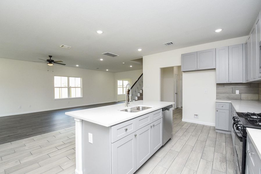 This is a spacious, modern kitchen with light-colored cabinets and countertops, featuring a central island with a sink. It has a gas stove, wood-look flooring, and ample natural light. The adjoining open-plan area allows for dining or living space, with a view of the staircase leading to the upper level. This is a spacious, modern kitchen with light-colored cabinets and countertops, featuring a central island with a sink. It has a gas stove, wood-look flooring, and ample natural light. The adjoining open-plan area allows for dining or living space, with a view of the staircase leading to the upper level.