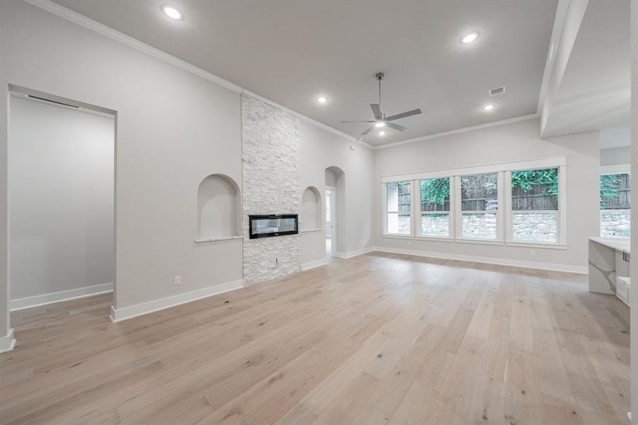 Unfurnished living room featuring ornamental molding, light wood-type flooring, a stone fireplace, ceiling fan, and arched walkways