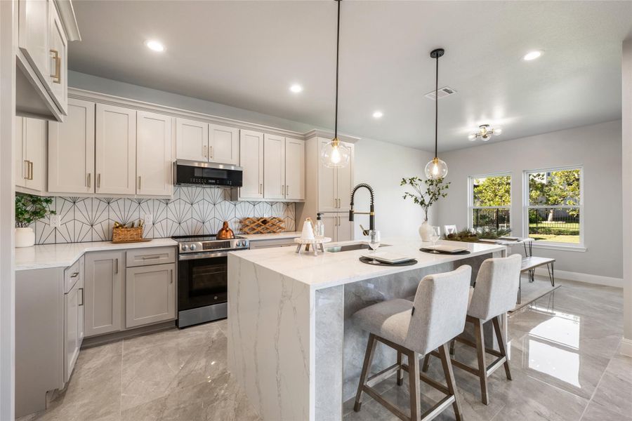 Kitchen featuring stainless steel range with electric stovetop, backsplash, light stone counters, a breakfast bar, and decorative light fixtures