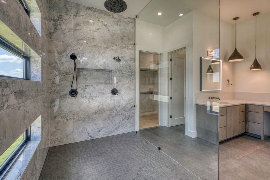 A glass-enclosed shower highlights marble wall tile alongside a sleek double vanity.