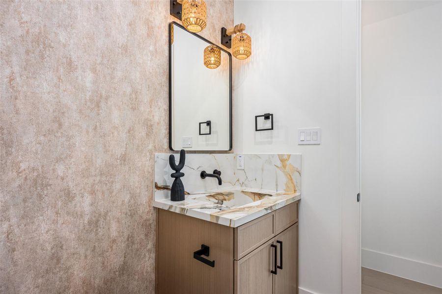 The guest bath features an onsite-crafted porcelain sink, accent mirror, luxe vanity lighting, and designer fixtures throughout