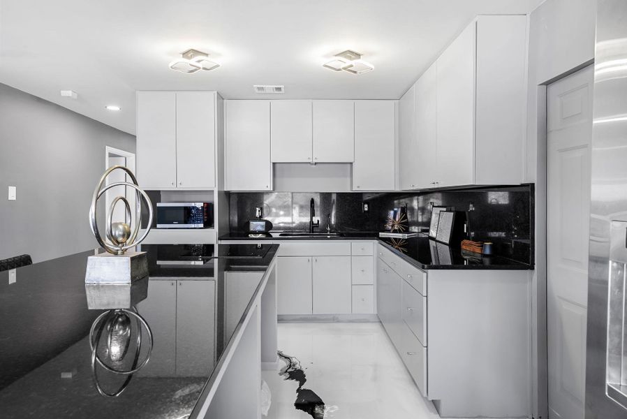 Kitchen featuring white cabinets, dark stone counters, tasteful backsplash, stainless steel appliances, and modern cabinets