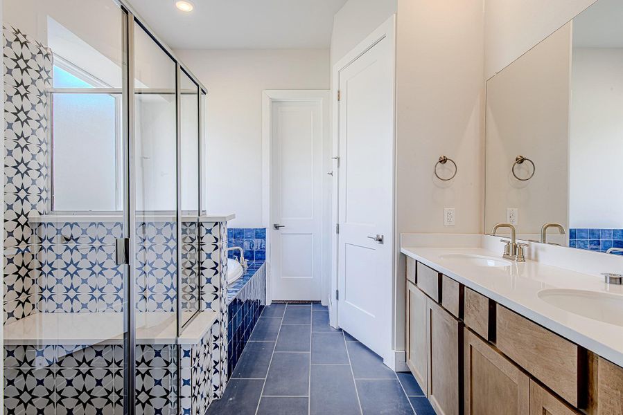 The primary bath features dual vanities, designer tile, a soaking tub, and a glass-enclosed shower—balancing statement style with everyday function.