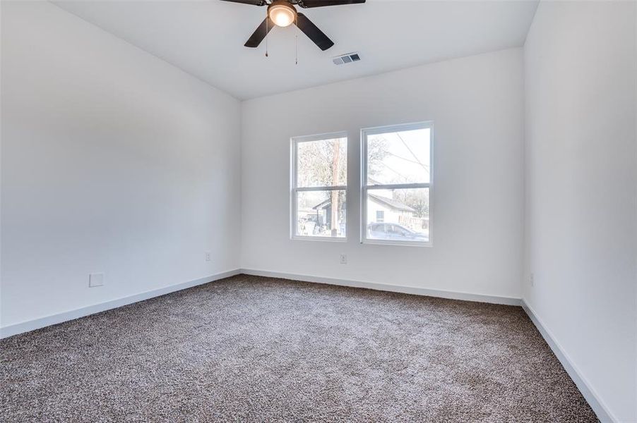 Carpeted spare room with baseboards, visible vents, and ceiling fan