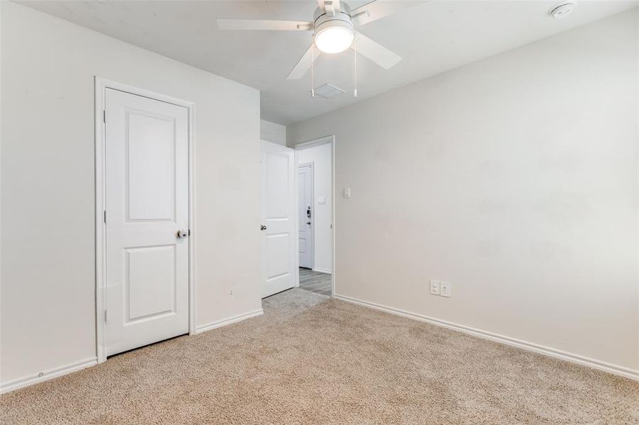 Carpeted room featuring a ceiling fan with integrated lighting, white baseboards, and a white two-panel interior door Carpeted room featuring a ceiling fan with integrated lighting, white baseboards, and a white two-panel interior door