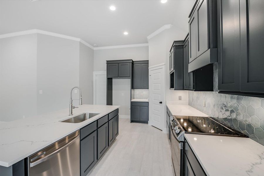 Kitchen with decorative backsplash, appliances with stainless steel finishes, ornamental molding, a sink, and light stone countertops