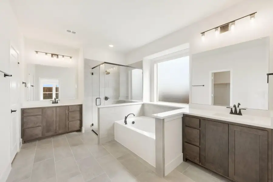 Master bathroom with dual vanities, soaking tub, and glass walk-in shower with tile floors