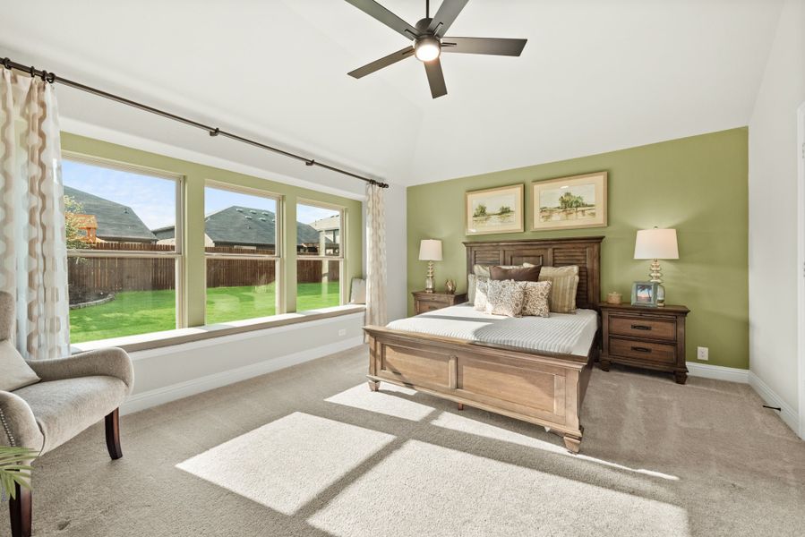 Bedroom with wood bed frame, green accent wall, ceiling fan, and large windows overlooking backyard