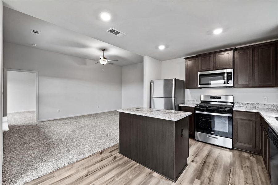 Kitchen with dark brown cabinets, ceiling fan, stainless steel appliances, light colored carpet, and a kitchen island