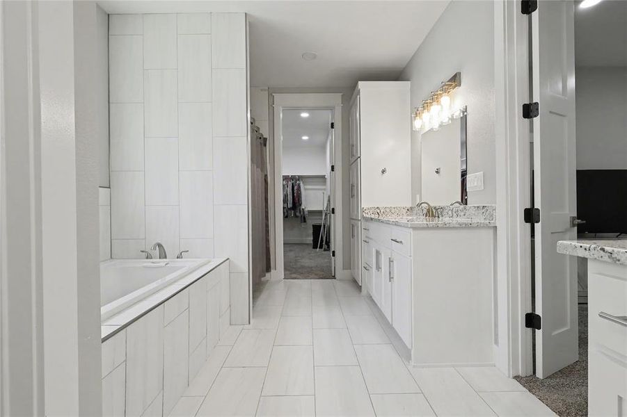 Modern bathroom featuring a built-in soaking tub, a single vanity with stone-finish countertop, and large format white tile flooring