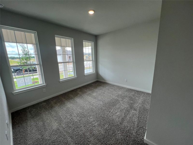 Three bright windows illuminate a versatile room with plush carpeting, perfect for a quiet retreat or productive workspace.