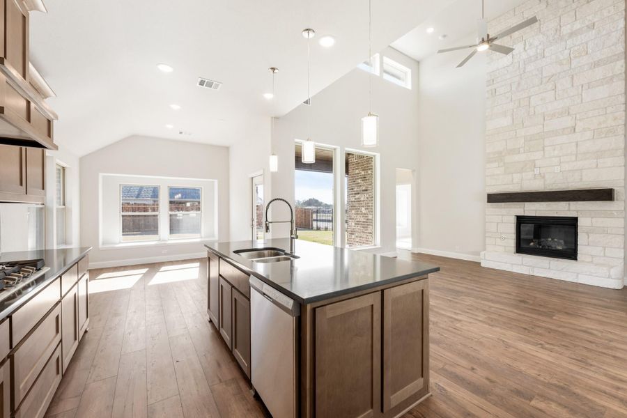 Open-concept kitchen with center island, dark countertops, and stone fireplace under vaulted ceiling Open-concept kitchen with center island, dark countertops, and stone fireplace under vaulted ceiling