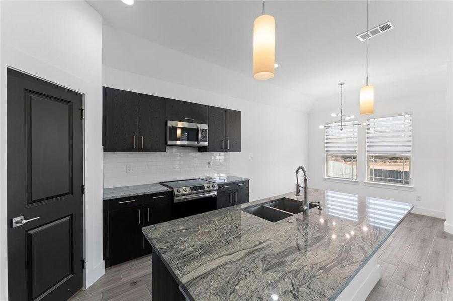 Kitchen with a center island with sink, sink, light hardwood / wood-style flooring, decorative light fixtures, and stainless steel appliances