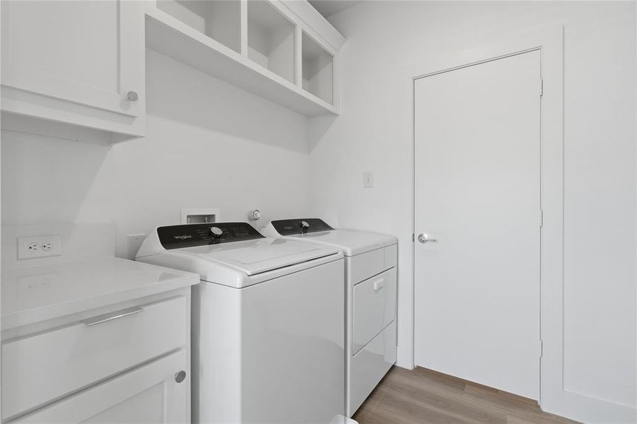Utility room featuring white cabinetry, open shelving, a solid surface countertop, wood-finish flooring, and a white door