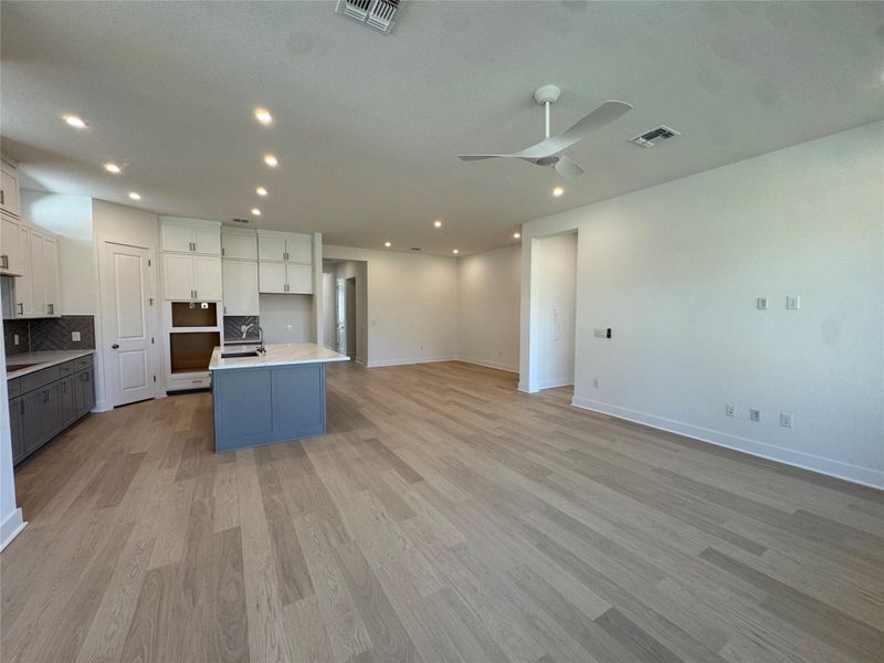 Kitchen featuring open floor plan, backsplash, an island with sink, light wood-style floors, and ceiling fan